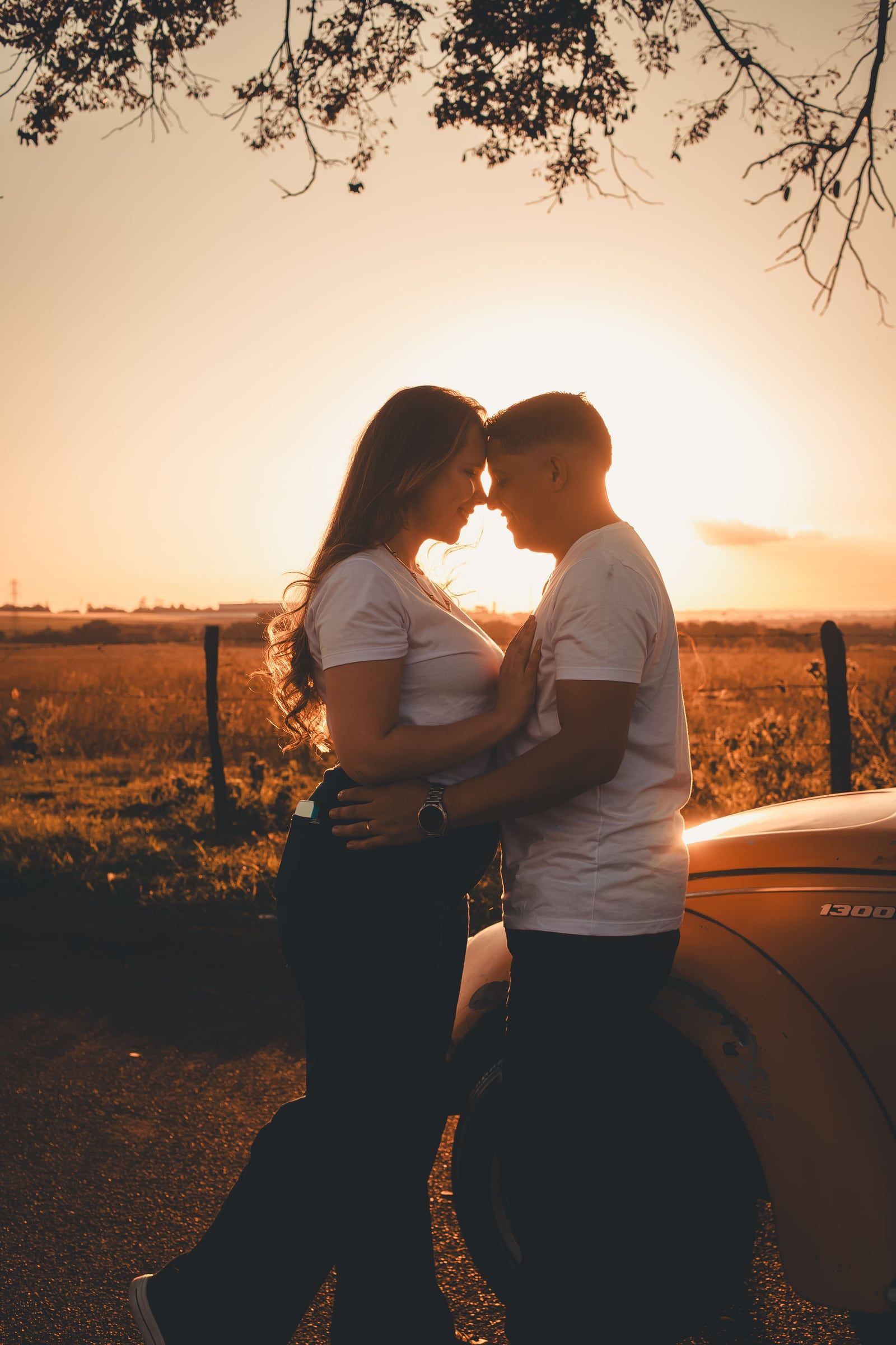 Casal testa com testa em contraluz, com o sol a pôr-se entre os dois.