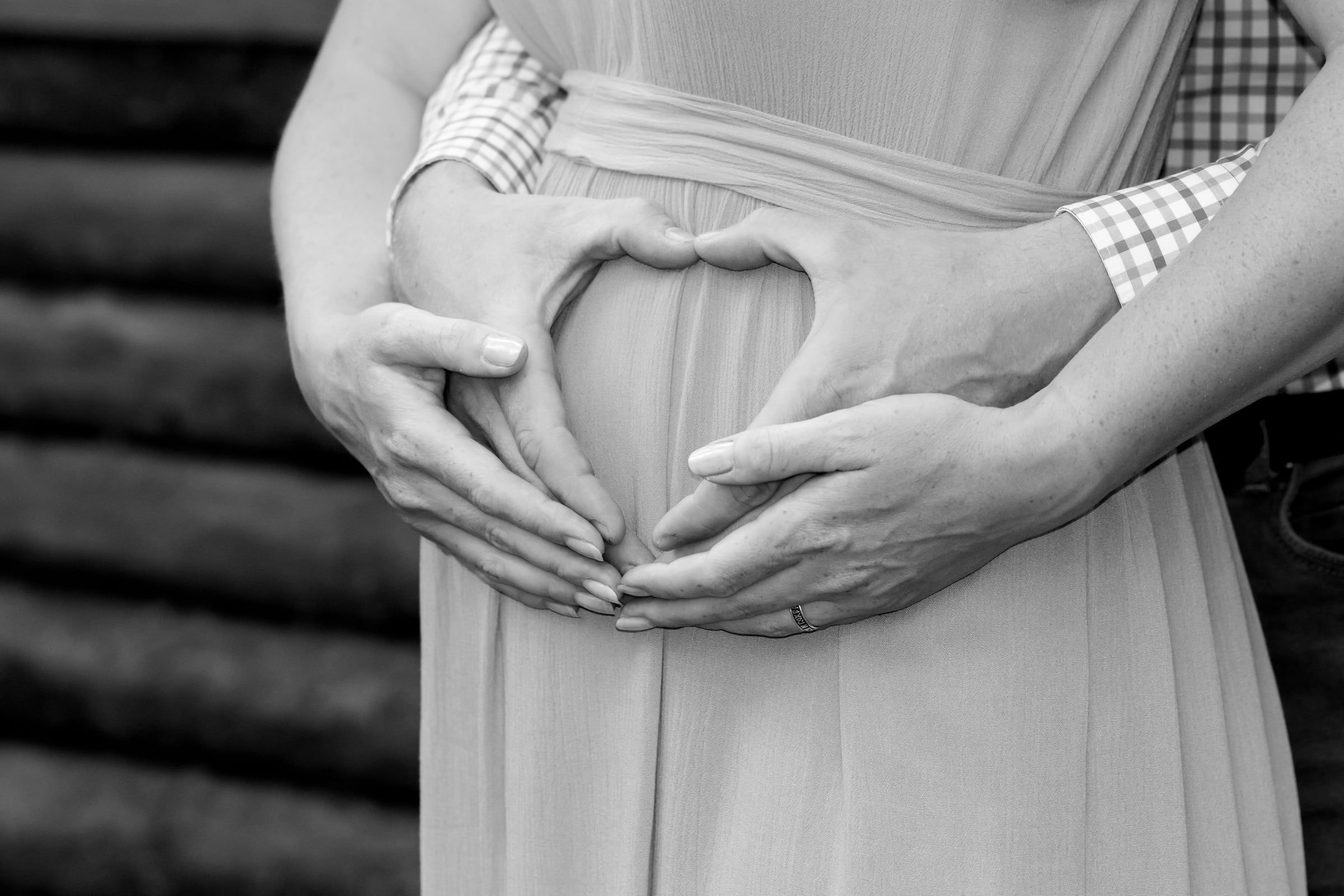 Duas mãos fazem um coração sobre um vestido claro.