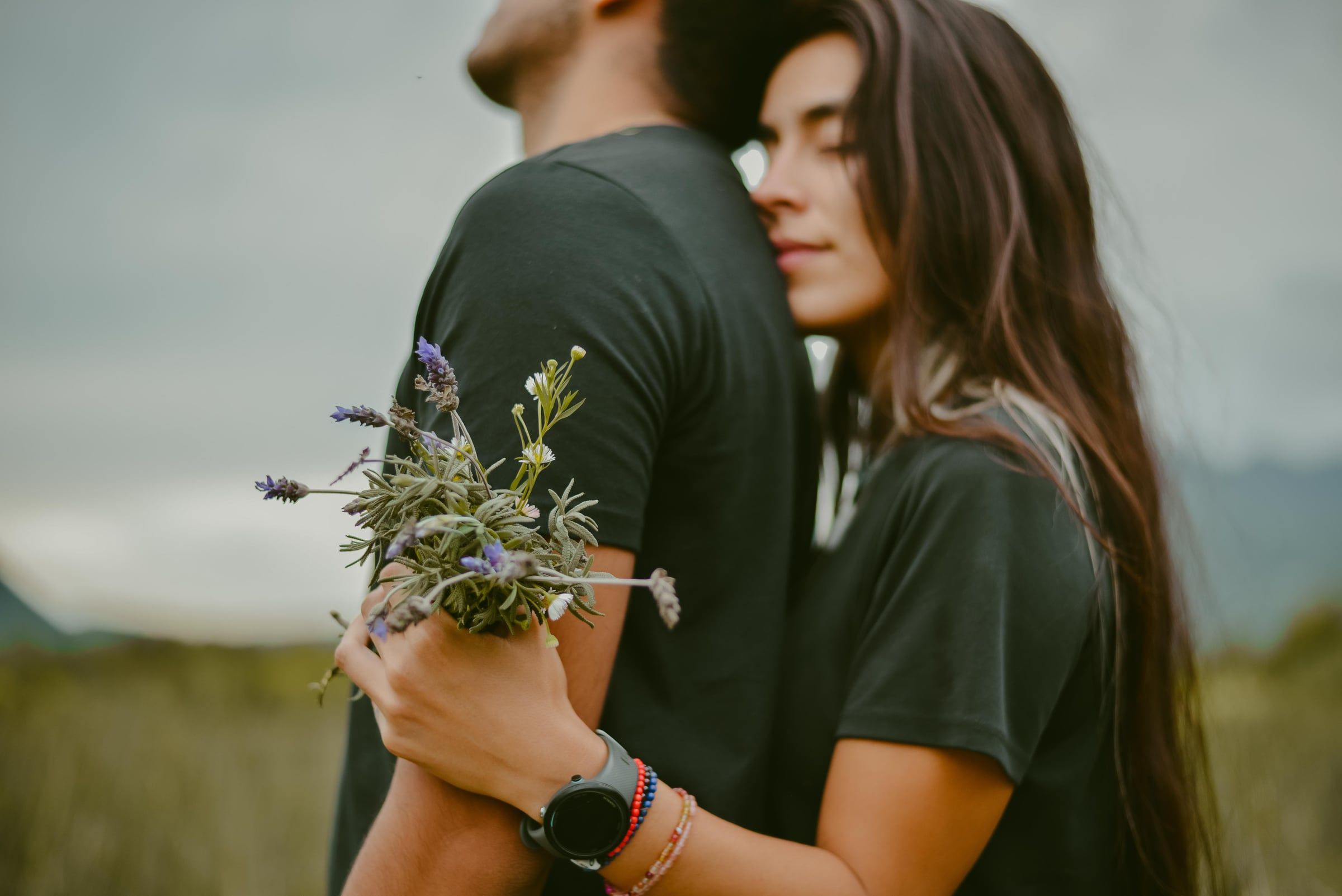 Ela abraça-o por trás com um ramo de flores do campo.
