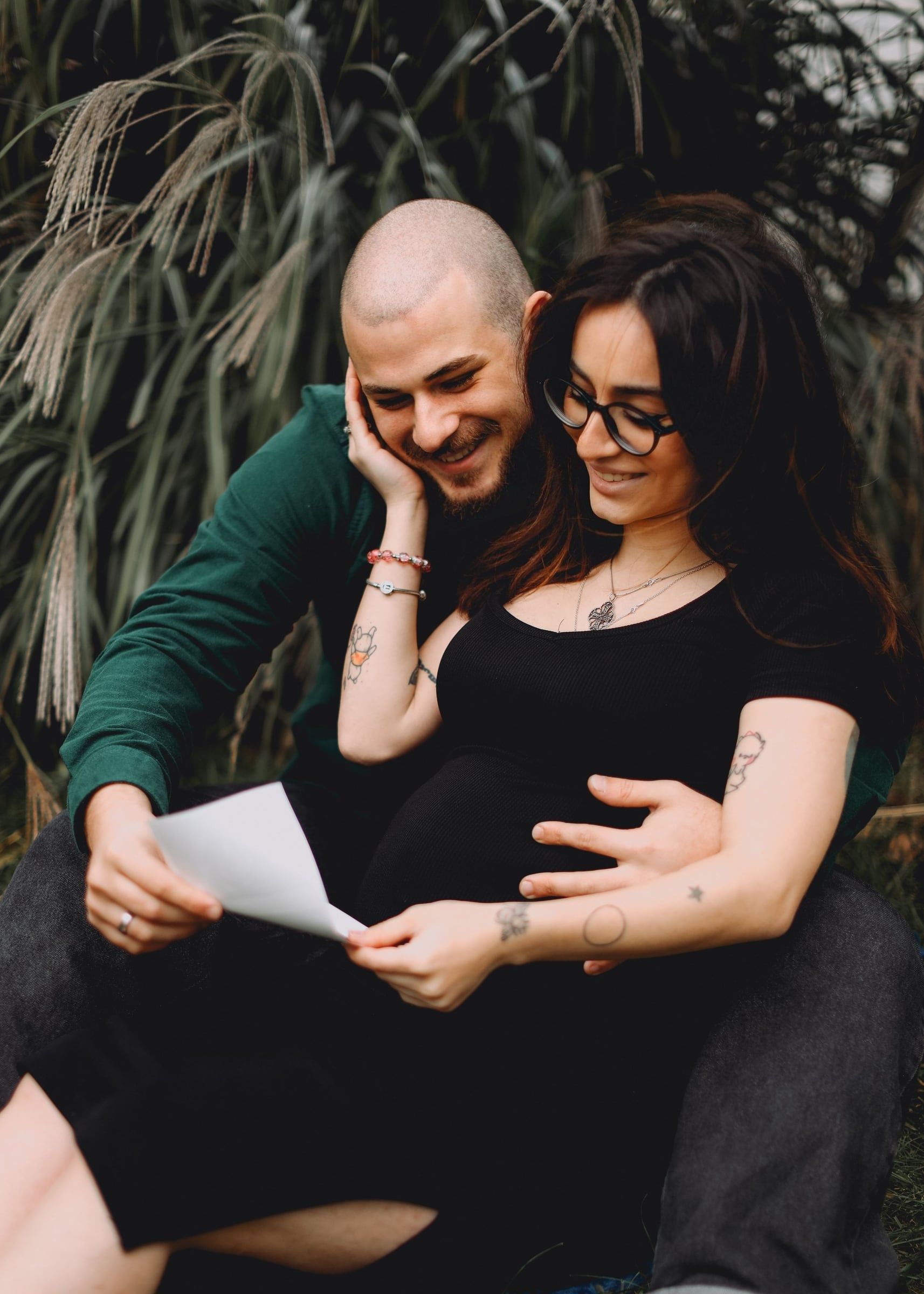 Casal sentado lado a lado a ler uma carta, ela com a mão na barriga.