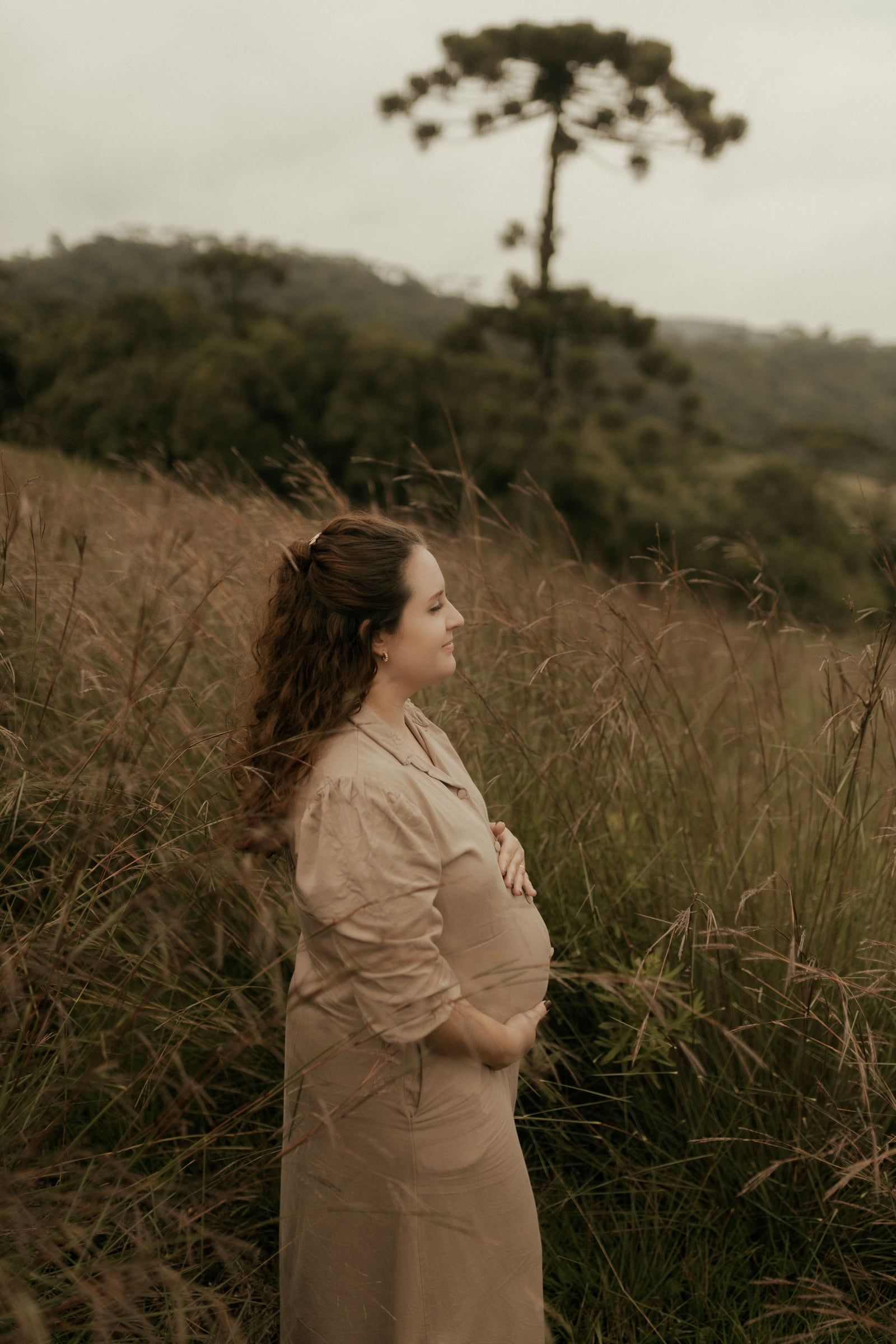 Mulher sozinha num campo de erva alta, de perfil.