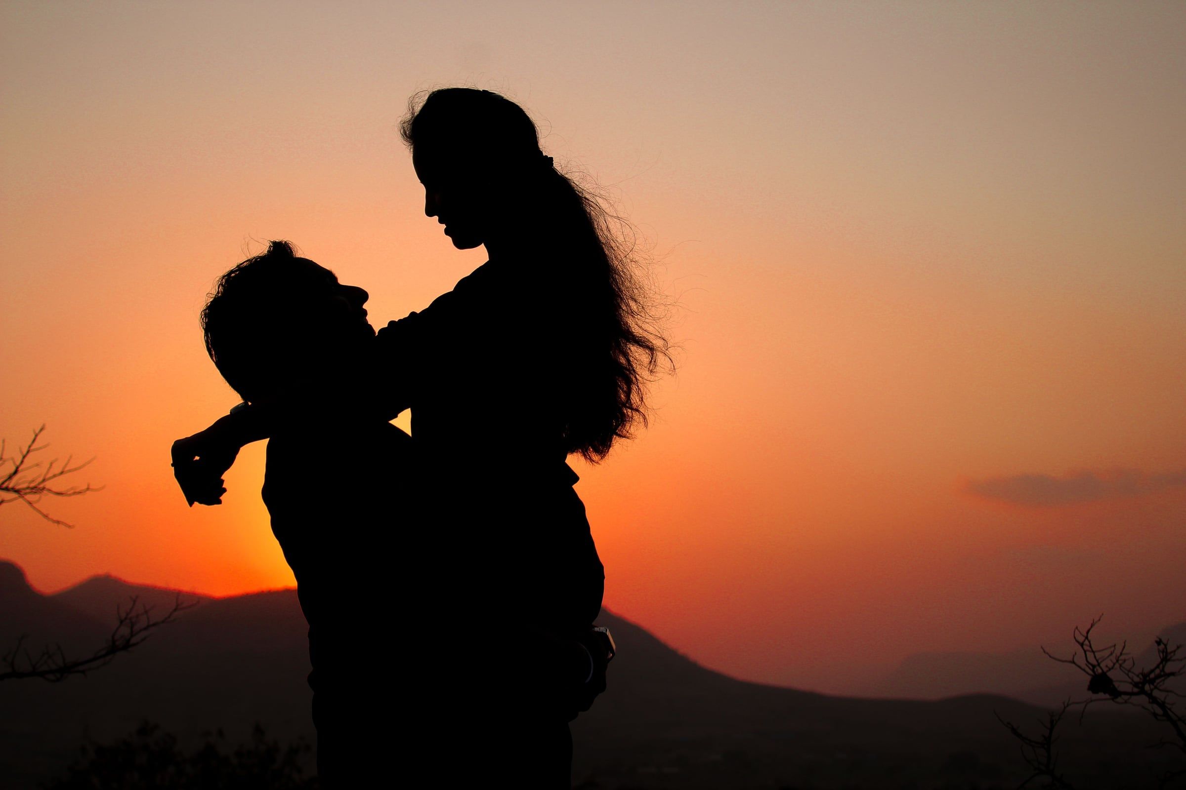Silhueta de uma mãe a levantar o filho ao pôr do sol.