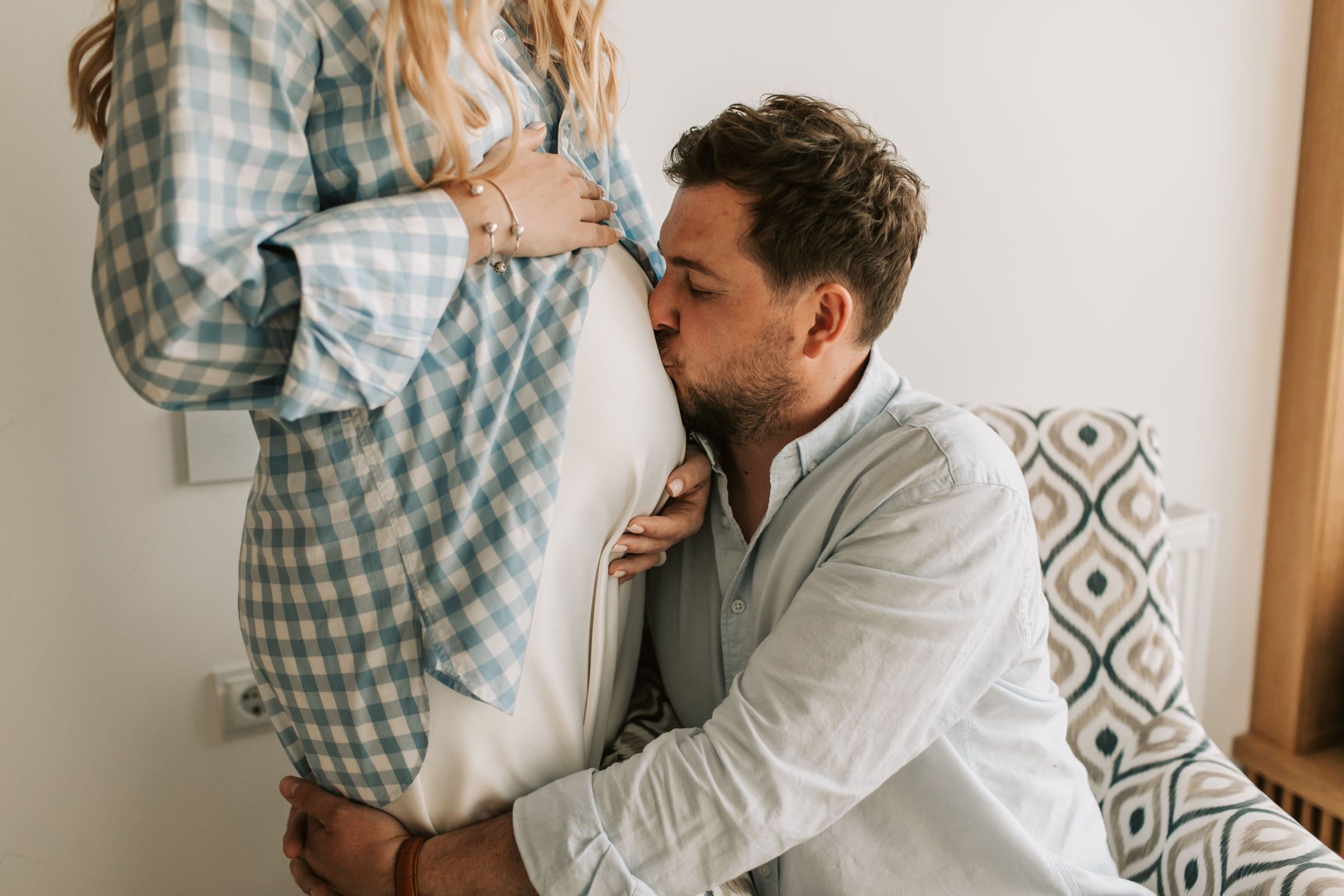Ele encosta a cara à barriga dela, sentados no sofá.